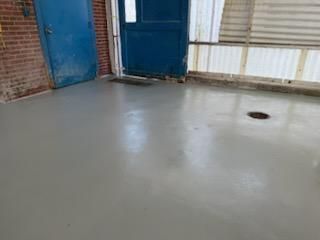 Gray, shiny floor in a room with a blue door, brick wall, and a window with white panels.