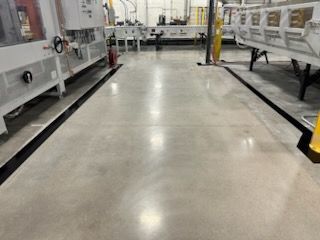 Factory floor with gray concrete, black painted borders, and machinery.