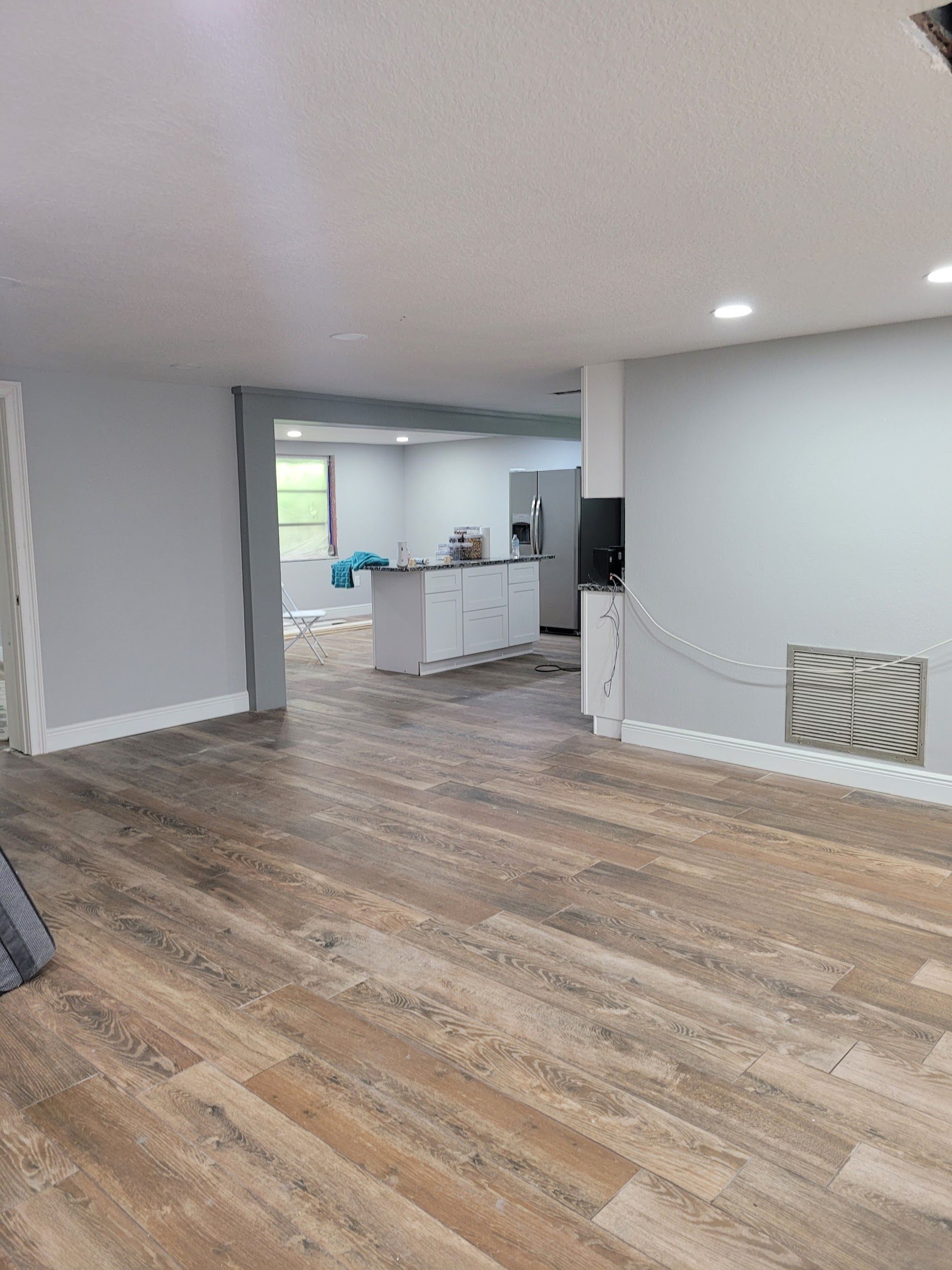 A large room with hardwood floors and a kitchen in the background.