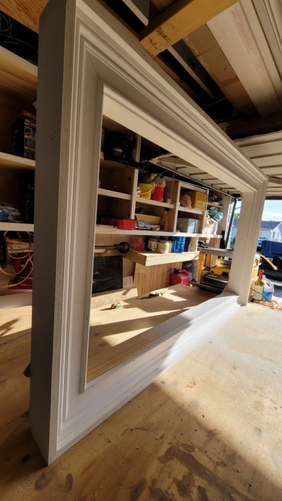 A large white frame is sitting on top of a wooden table in a garage.