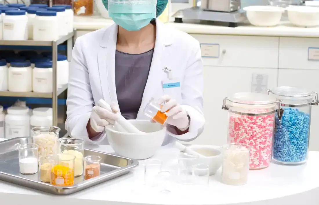Un pharmacien en blouse blanche mélange des ingrédients au mortier et au pilon, entouré de bocaux contenant des substances colorées.