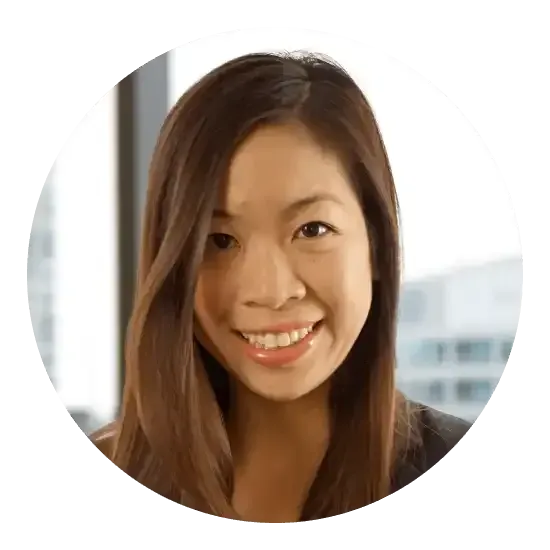 Femme souriante aux longs cheveux bruns, vêtue d'un haut foncé, regardant l'objectif dans un bureau lumineux.