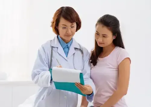 Un médecin en blouse blanche examine un dossier avec une patiente en chemise rose.