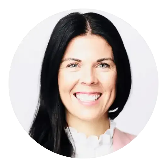 Femme aux cheveux foncés souriante, vêtue d'un blazer rose et d'un chemisier blanc, sur fond clair.