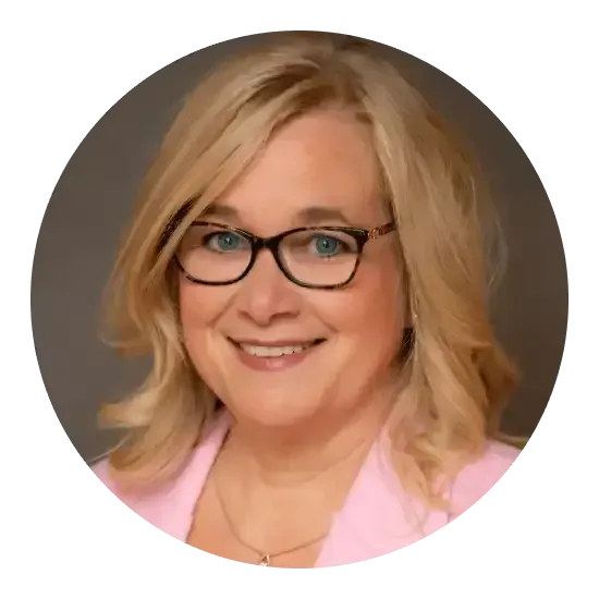 Femme blonde, portant des lunettes et un blazer rose, souriante.