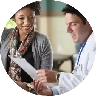 Une femme et un médecin examinent ensemble des documents ; le médecin montre du doigt en souriant.