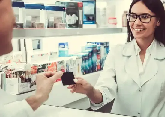 Un pharmacien accepte une carte au comptoir de son officine. Le pharmacien sourit.