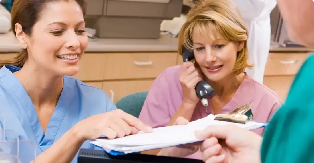 Personnel médical dans la salle d'attente. Une infirmière désigne des documents, une autre répond au téléphone et une troisième tient des dossiers.