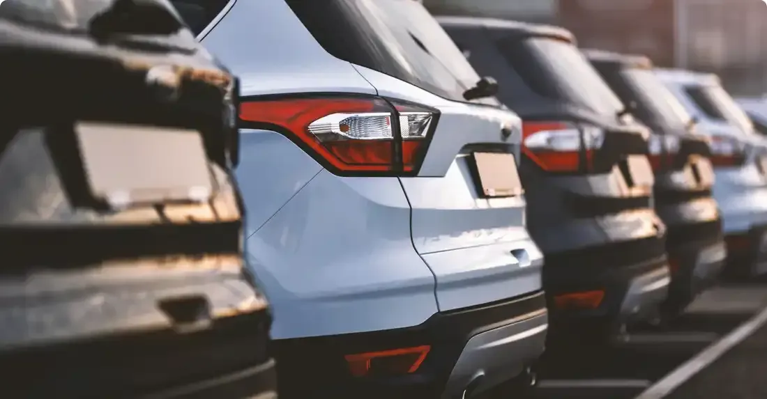 Rangée de SUV stationnés, feux arrière allumés. Couleurs variées : blanc, noir et argent. À l’extérieur, probablement sur le parking d’une concession automobile.