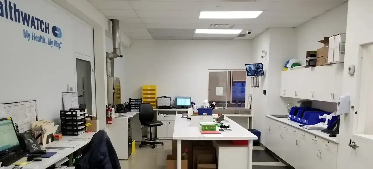 Intérieur d'un laboratoire avec des armoires, des bureaux et du matériel blancs, et le logo Healthwatch sur le mur.