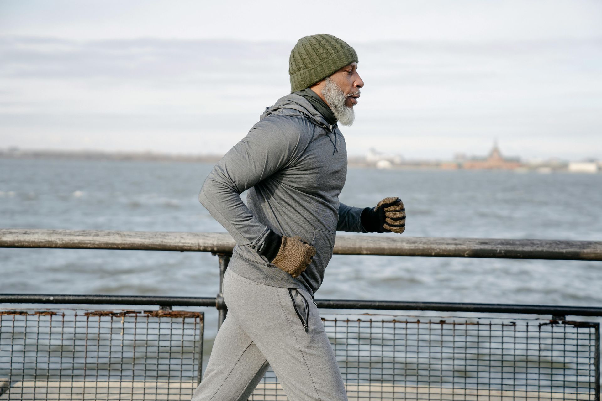 A man with a beard is running on a pier near the water.