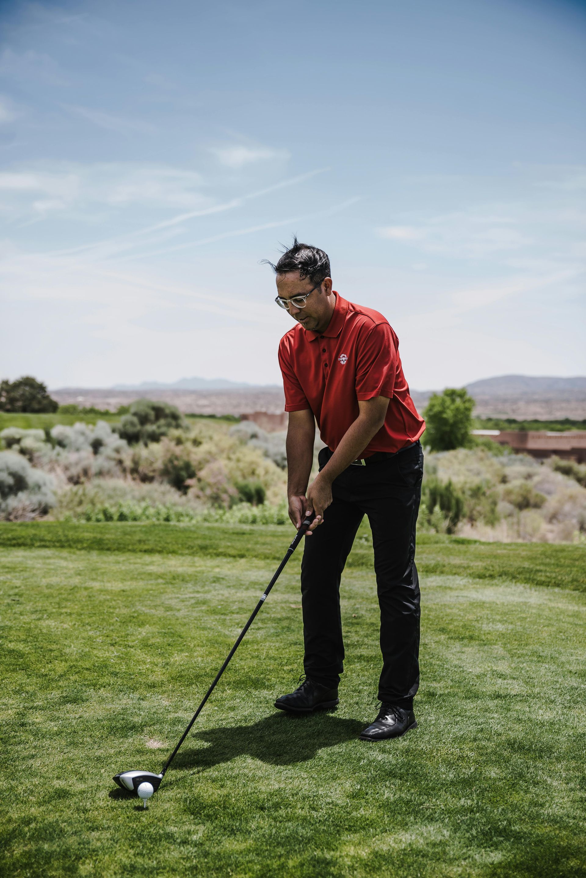 A man in a red shirt is swinging a golf club on a golf course.