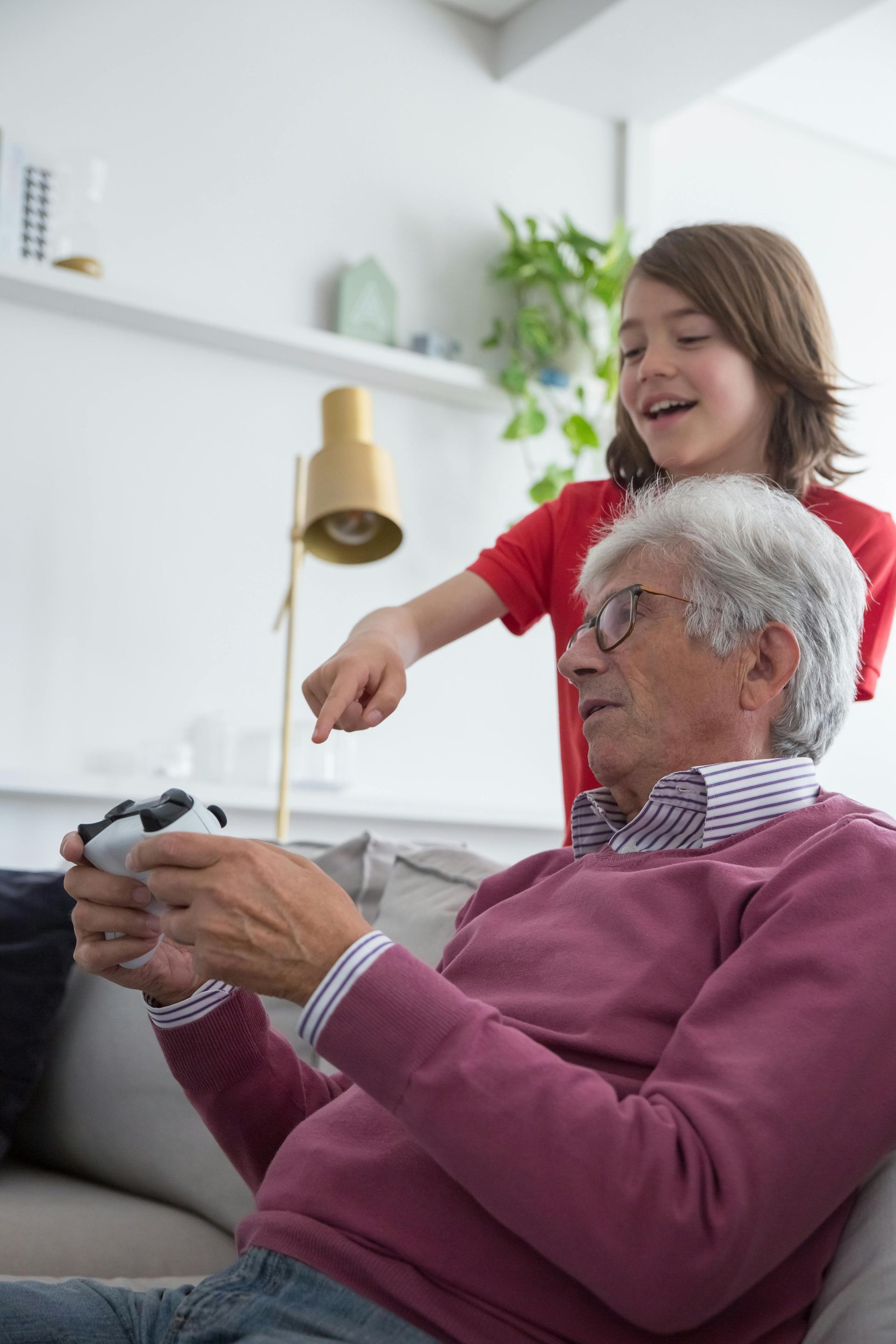 An elderly man is sitting on a couch playing a video game with his grandson.