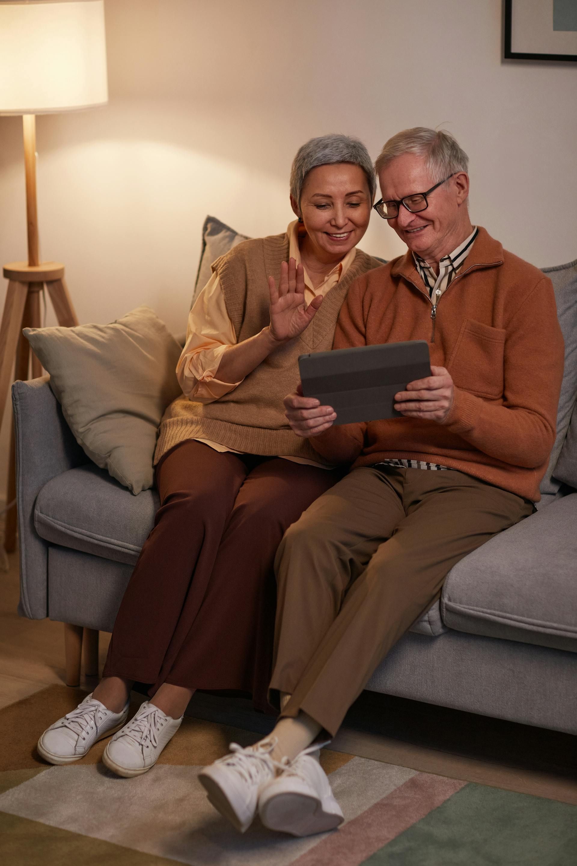 An elderly couple is sitting on a couch looking at a tablet.