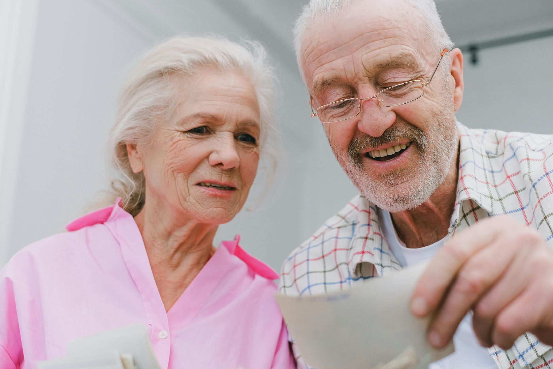 Two smiling seniors looking at a photo together, one holding the paper in a bright setting