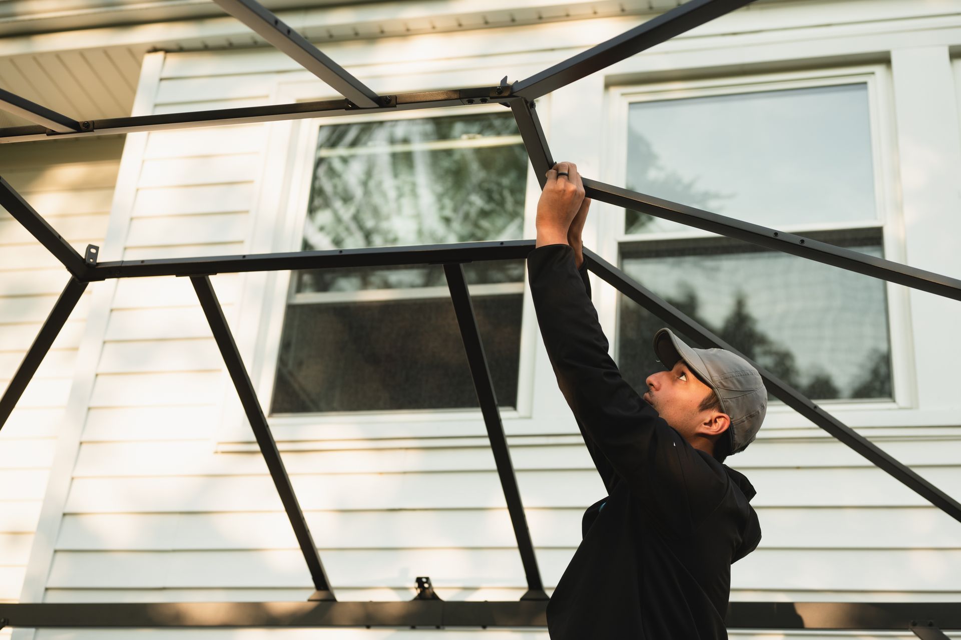 A man is working on a metal structure outside of a house.