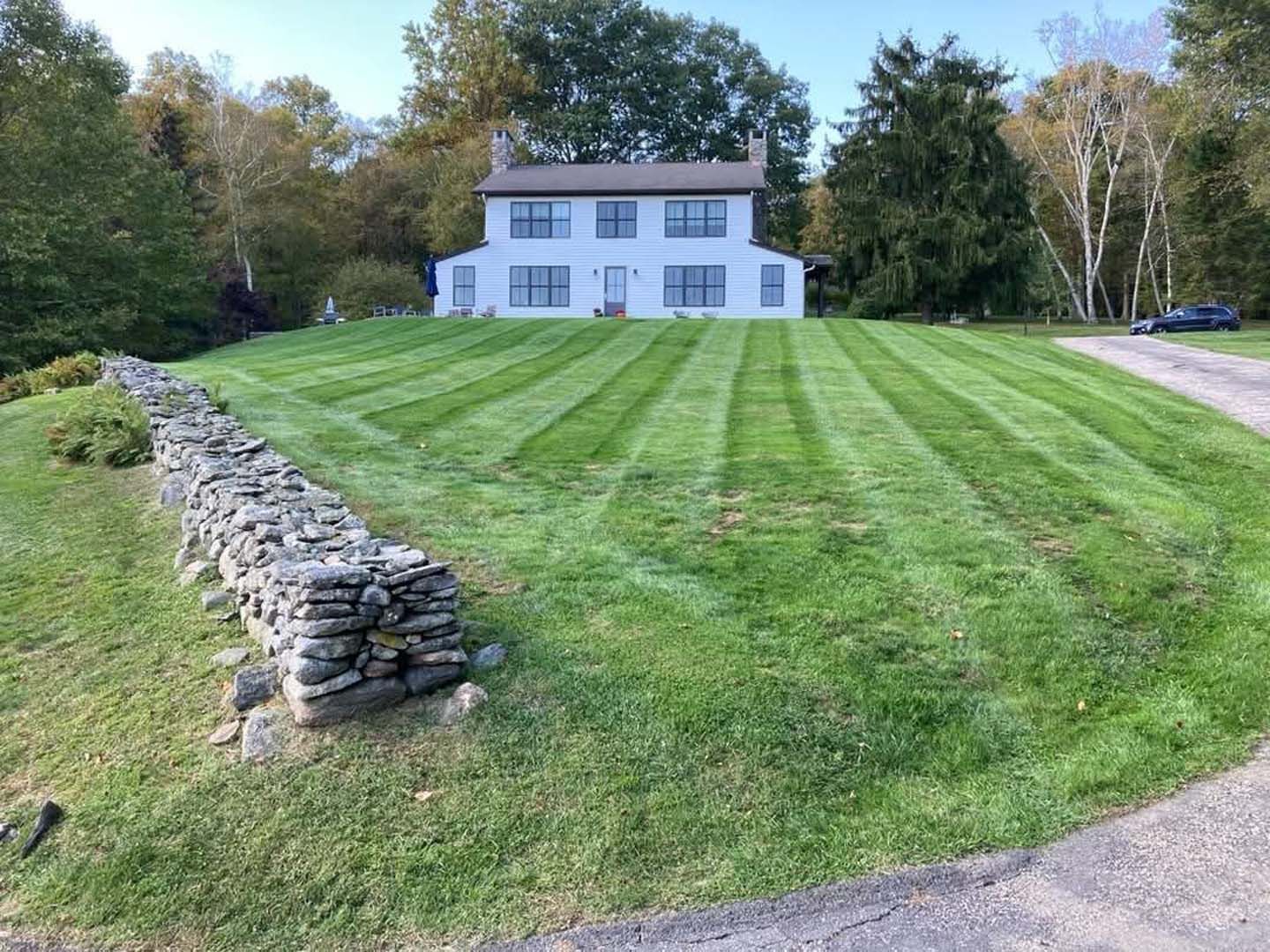 A large white house with a lush green lawn and a stone wall in front of it.