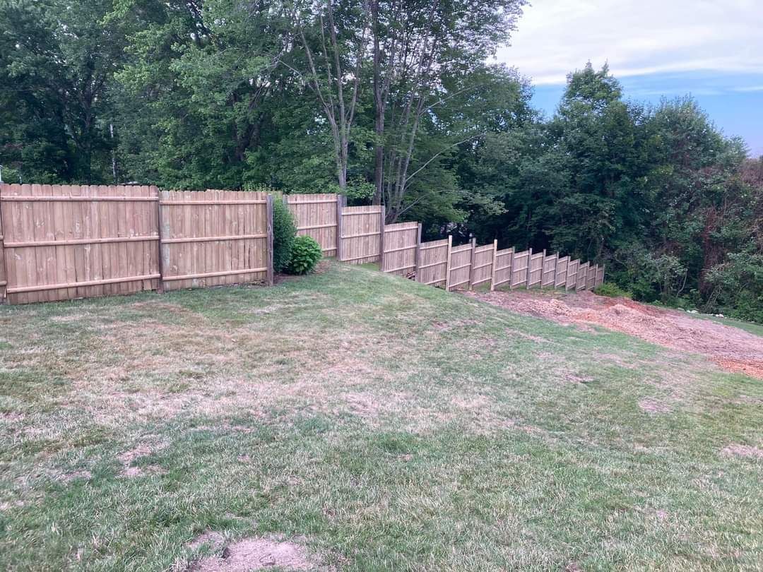 A wooden fence is sitting on top of a grassy hill next to a dirt road.