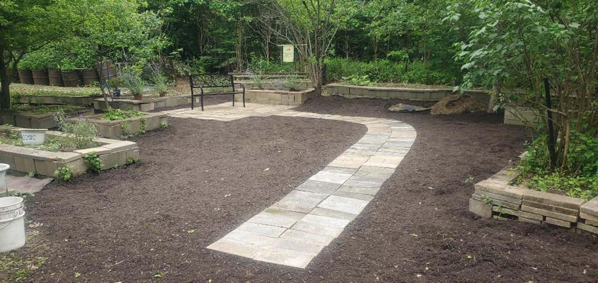 A stone walkway going through a garden surrounded by trees.