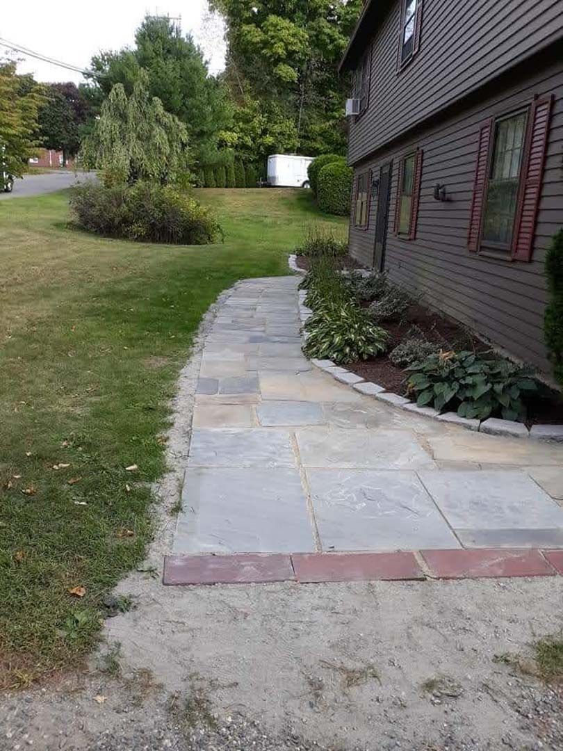 A stone walkway leading to a house with a brick border.