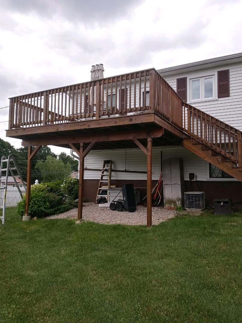 A wooden deck with stairs leading up to it is in the backyard of a house.