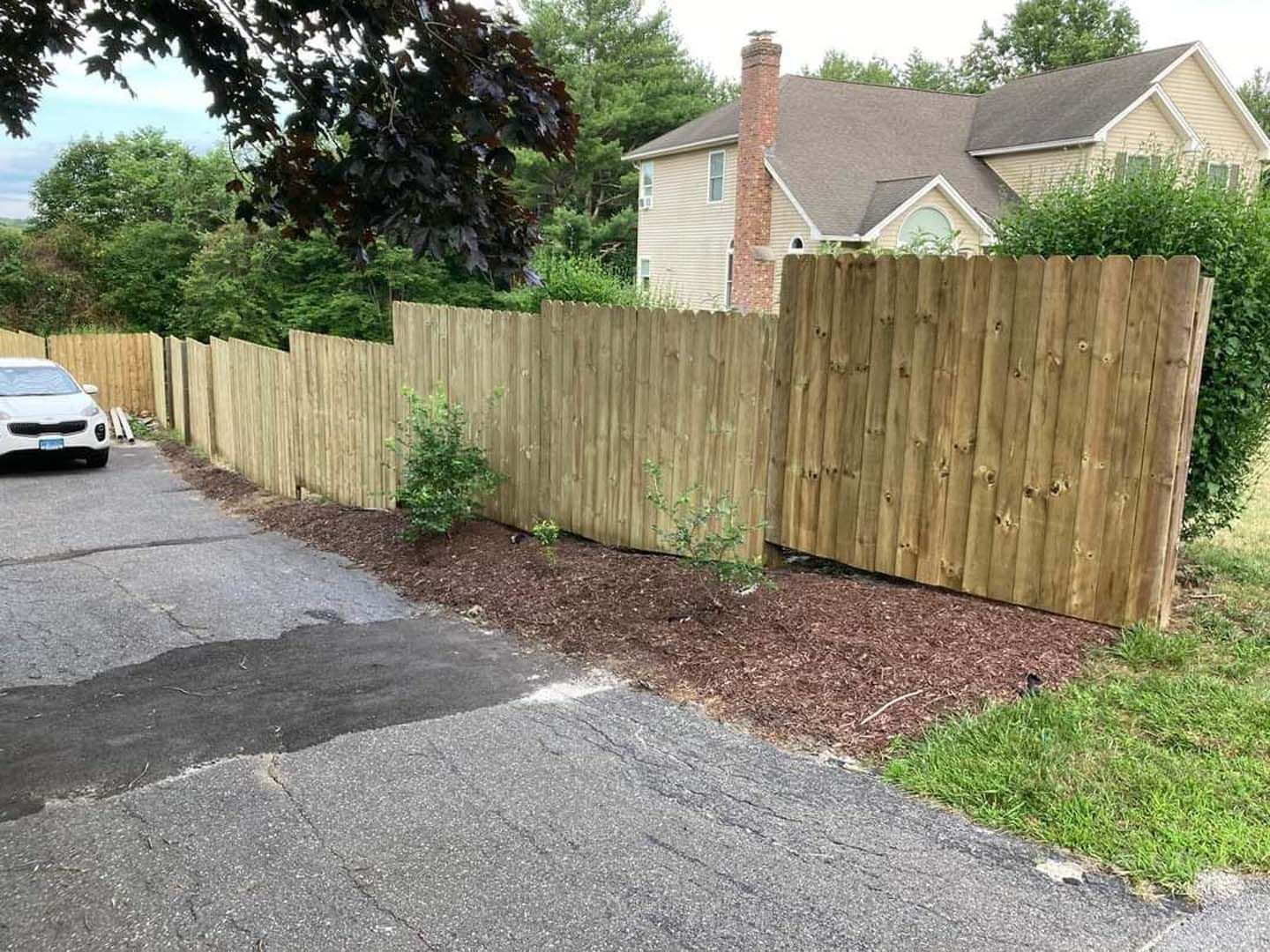 A car is parked next to a wooden fence in front of a house.