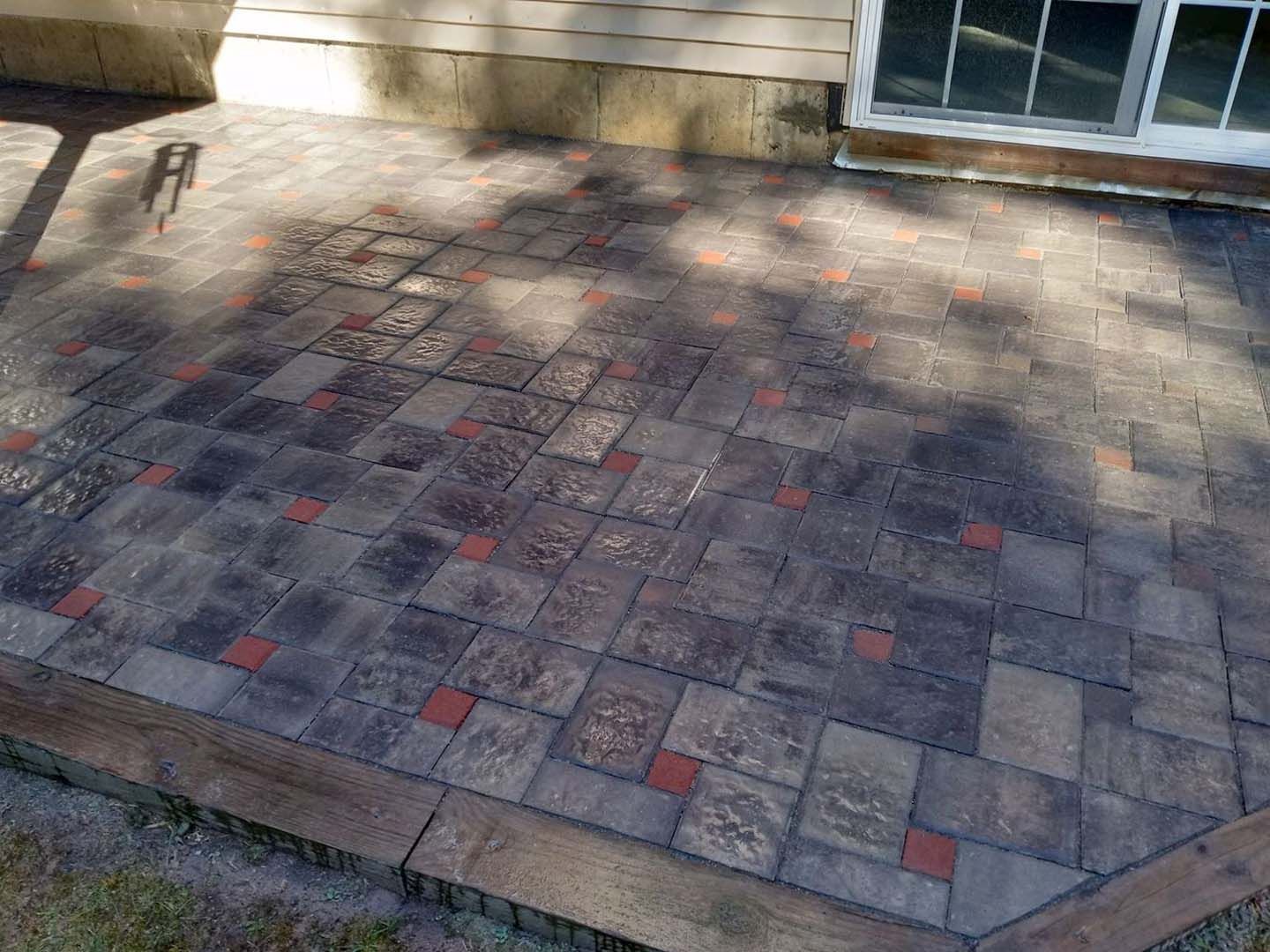 A patio with bricks and a wooden border is in front of a house.