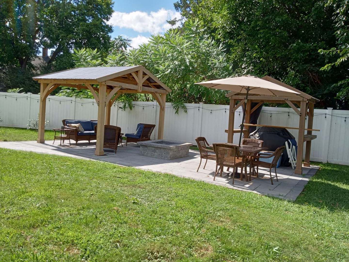 A backyard with a gazebo , table and chairs and a fire pit.
