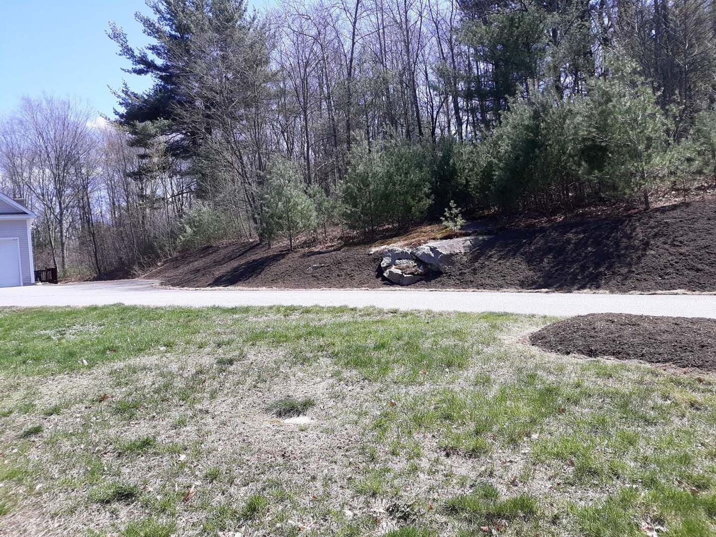 A grassy hillside with trees and a garage in the background.