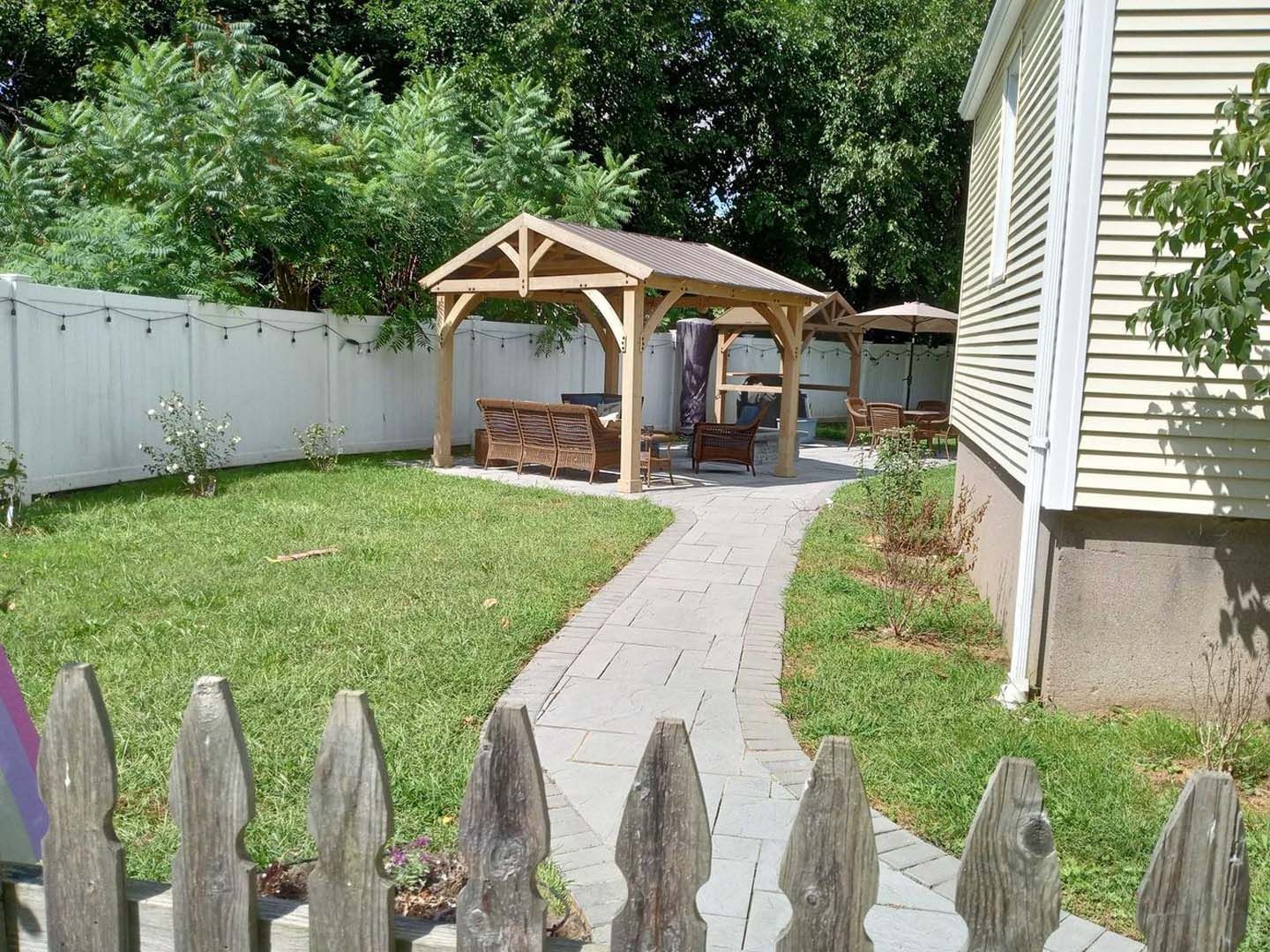 There is a wooden gazebo in the backyard of a house.