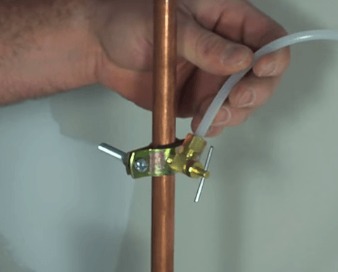 Hand attaching a clear tube to a copper pipe with a clamp and valve.