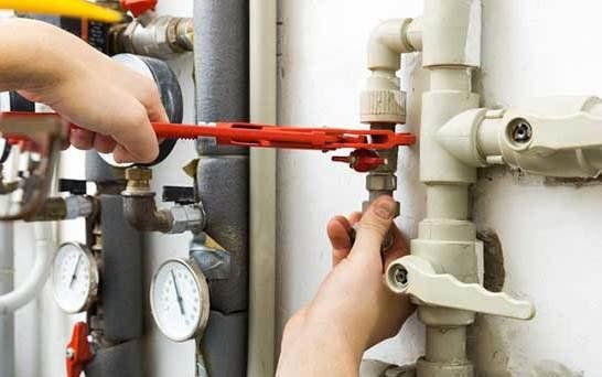 Person using a wrench on plumbing pipes, likely fixing a leak or performing maintenance.