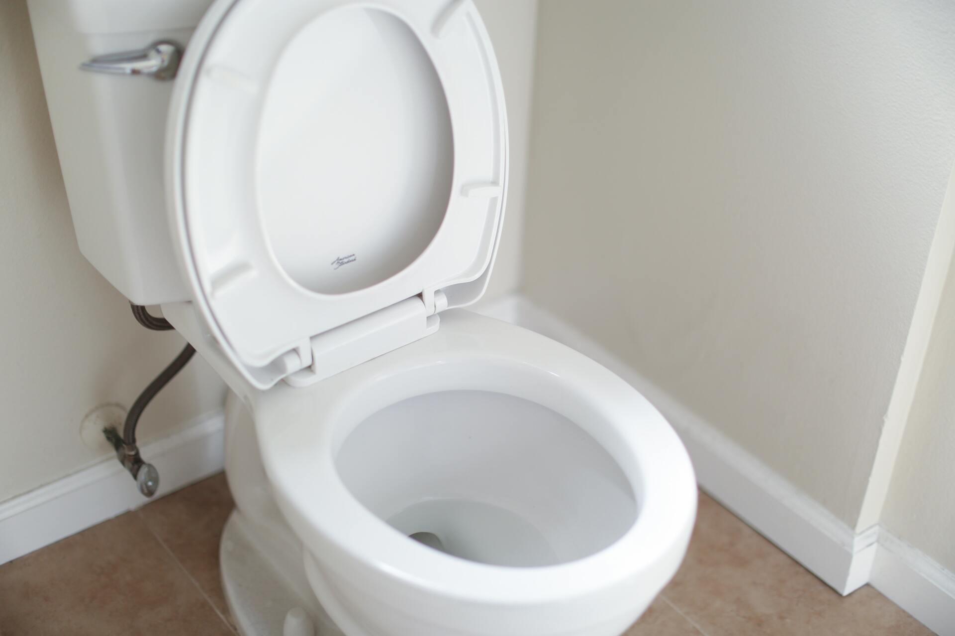 White toilet with the lid and seat raised in a room with beige walls and a beige floor.