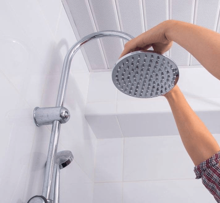 Person attaching a chrome showerhead to a curved arm in a white tiled shower.