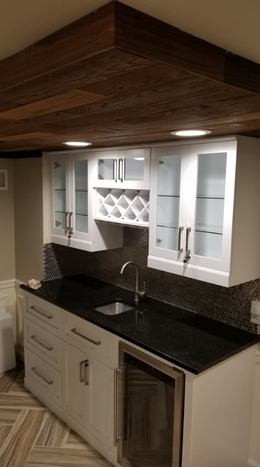 A kitchen with white cabinets , black counter tops , a sink , and a wine cooler.