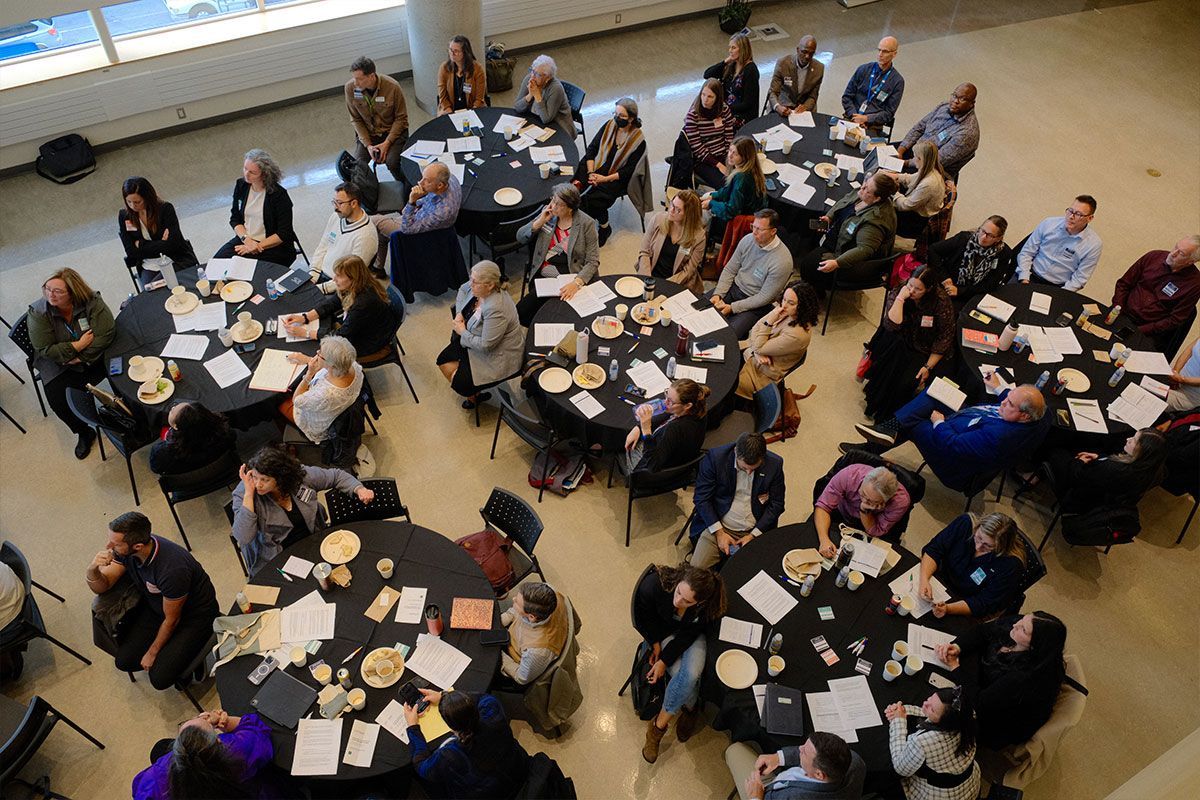 Un grand groupe de personnes sont assises à des tables rondes dans une pièce.