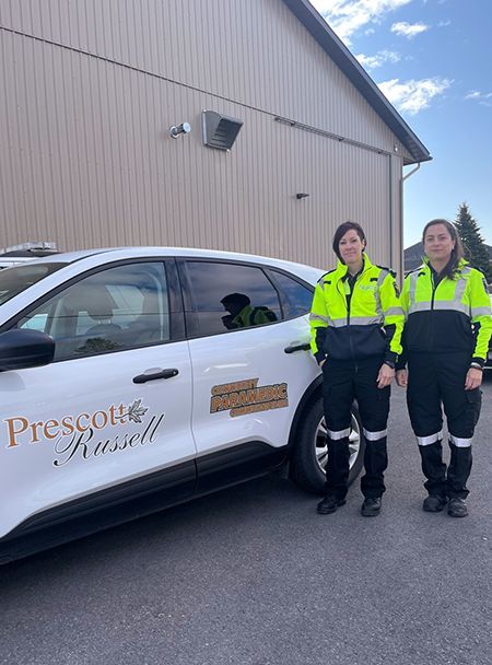 two female paramedics are standing in front of a car that says prescott russell