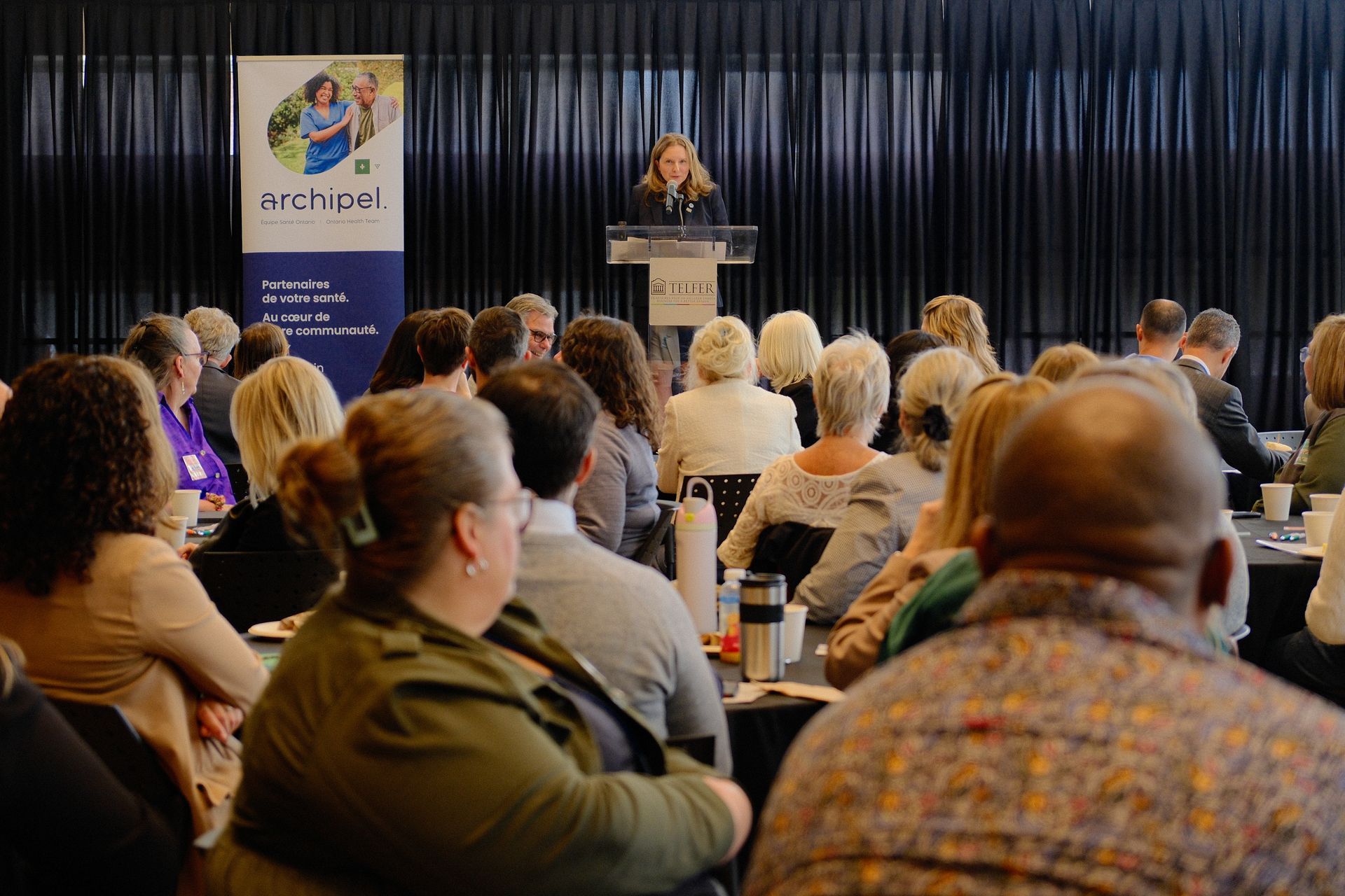 A woman is giving a speech to a large group of people at a conference.