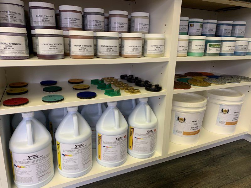 Shelves of pigment jars, resin, and samples. Jars are white with labels. Samples are colorful discs and figures.