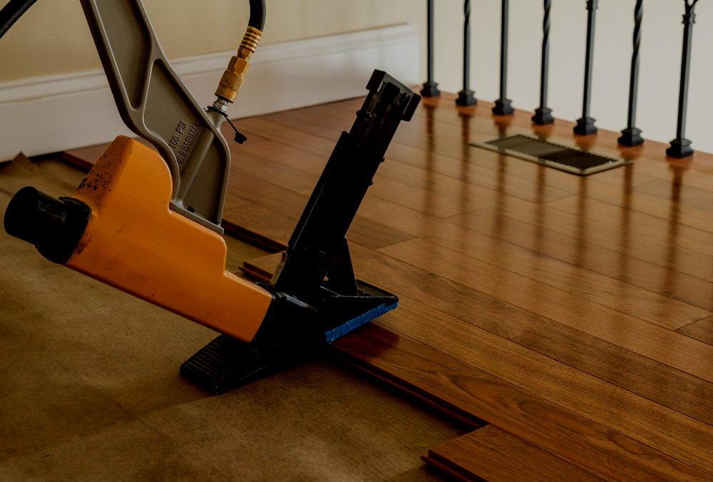 A nail gun is used to install hardwood flooring in a home.