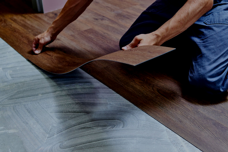 Person installing wood-look vinyl flooring over existing gray floor.