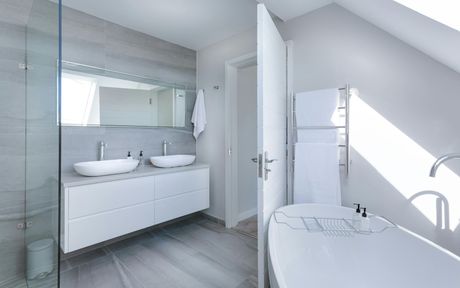 Bright white bathroom with double sinks, large mirror, bathtub, and towel rack.