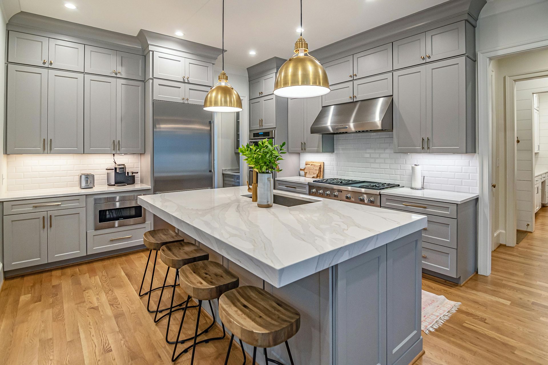 Gray kitchen with island, gold pendant lights, wood stools, stainless steel appliances, and white countertops.