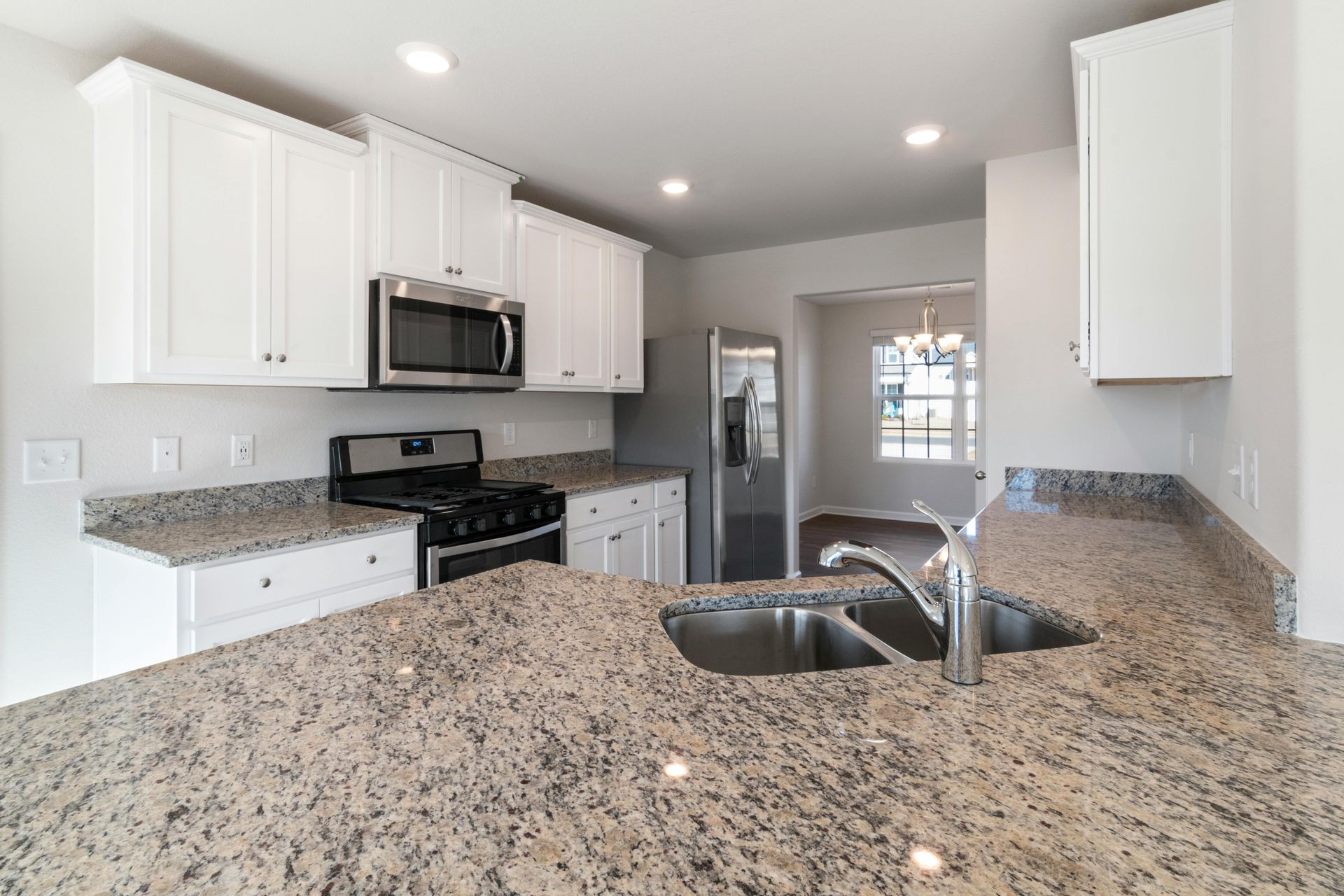 White kitchen with granite countertops, stainless steel appliances.