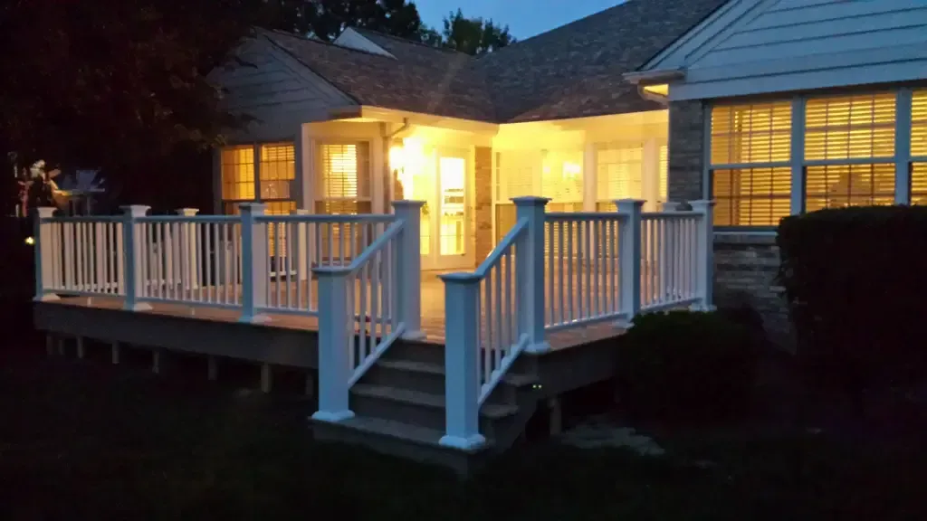 A house with a large deck and stairs is lit up at night.