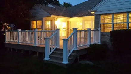 A house with a large deck and stairs is lit up at night.