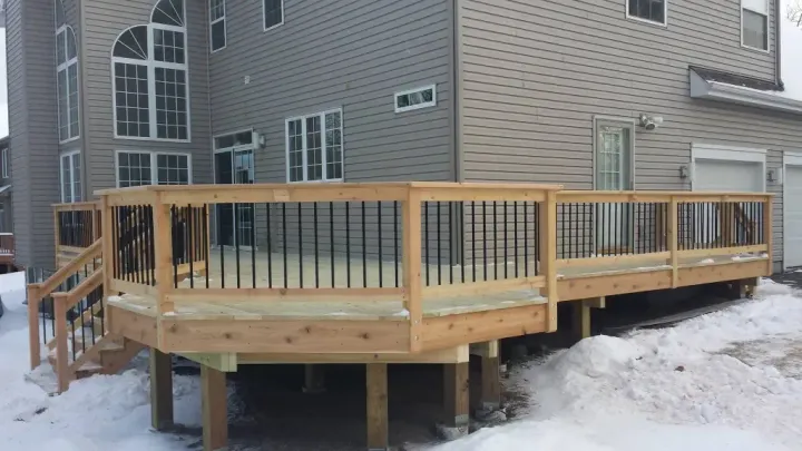 A large wooden deck is sitting in front of a house in the snow.
