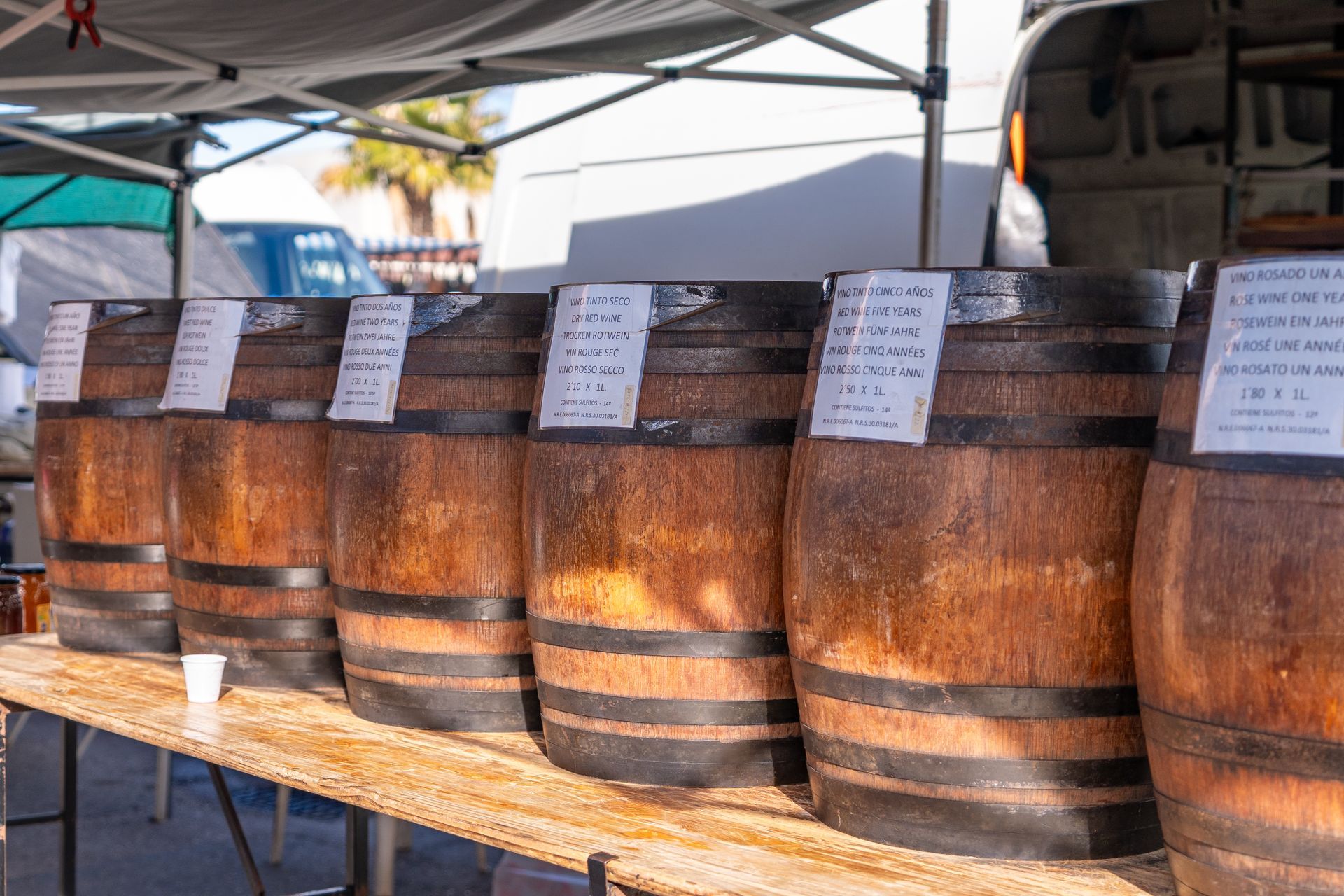 Wooden barrels with labels on a table at an outdoor market.