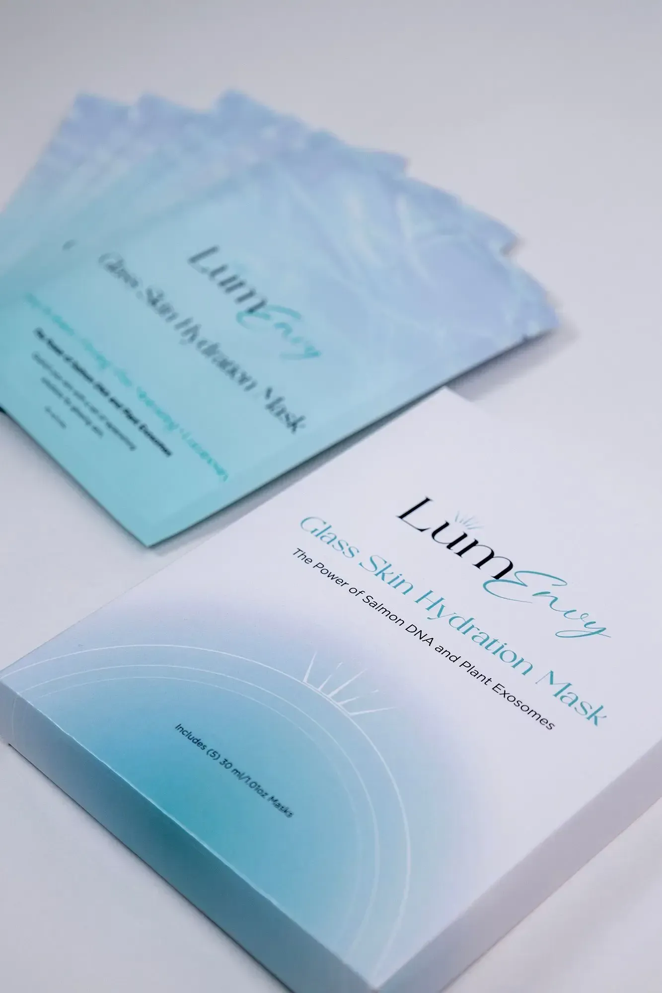 A Lumifay Glass Skin Hydration Mask box sits on a white surface with several matching blue mask packets fanned behind it.