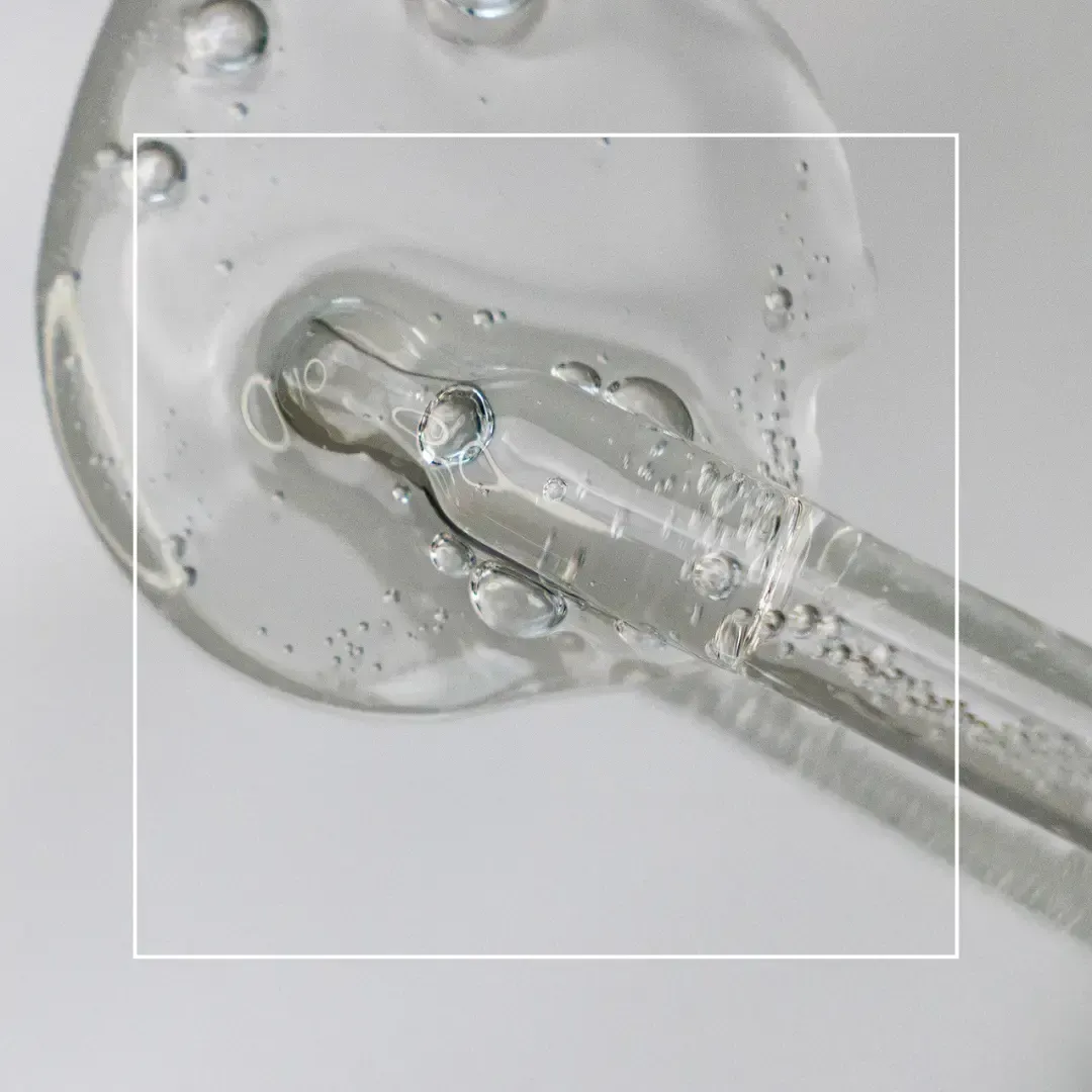 A clear glass dropper holding a glob of thick, transparent serum against a light gray background.